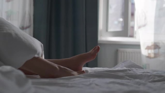 睡在床上的女人盖着白色的毯子，美丽的光脚被阳光照亮