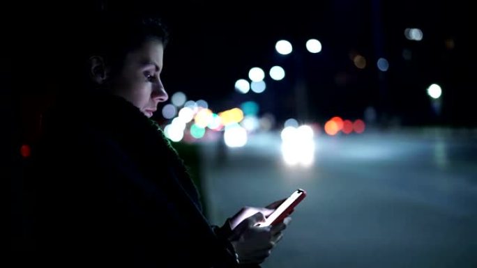 背景上使用智能手机和夜城的年轻女性的侧视图
