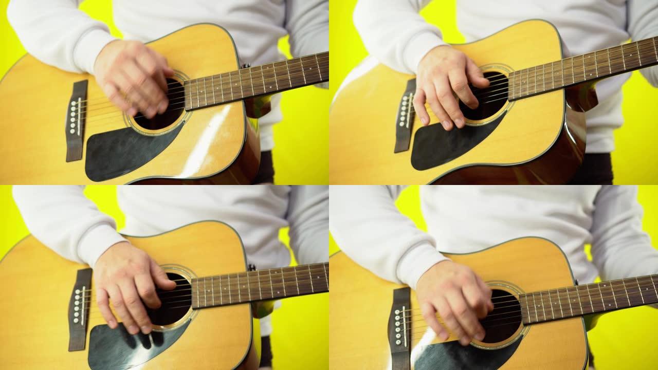 一个男人弹吉他的手的特写。一个穿着白色运动衫的男人的手弹吉他。黄色普通背景