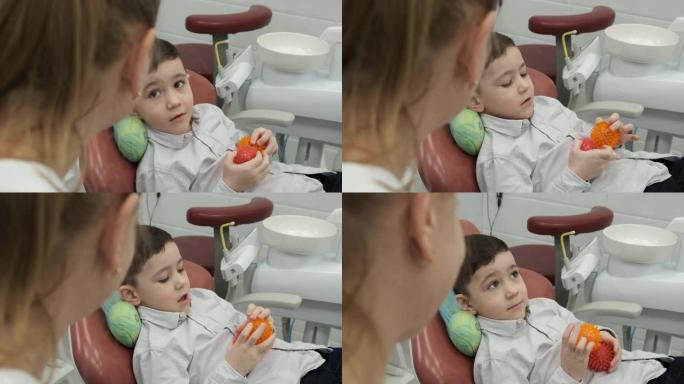 小男孩害羞接待口腔医生。男孩笑不担心牙科治疗，因为他的手里拿着两个橡皮球。医生正在和病人谈话，孩子不
