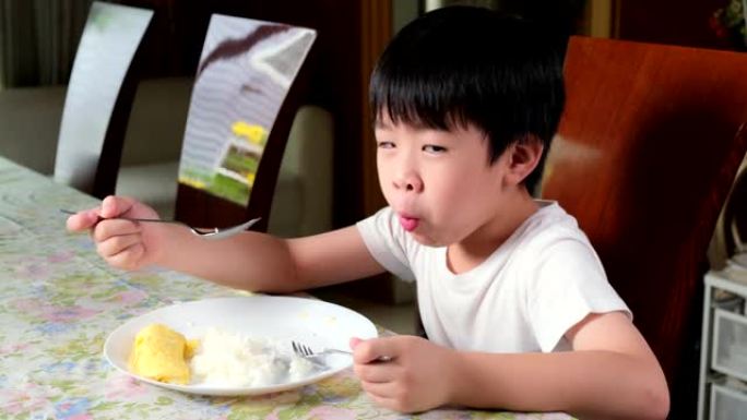 穿着白色t恤的年轻亚洲男孩早上在客厅的桌子上吃煎蛋卷