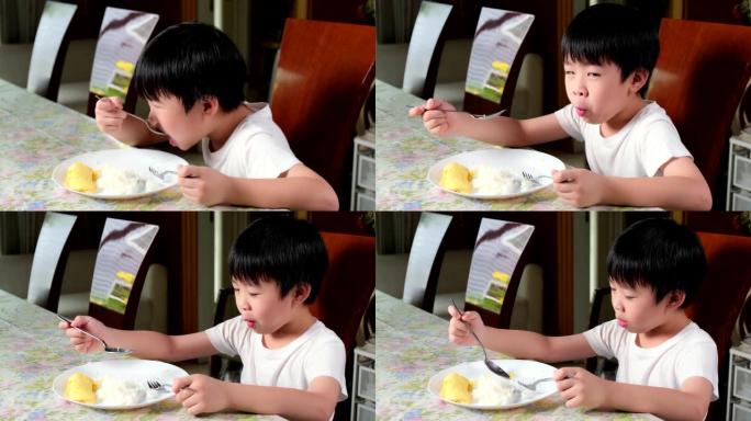 穿着白色t恤的年轻亚洲男孩早上在客厅的桌子上吃煎蛋卷