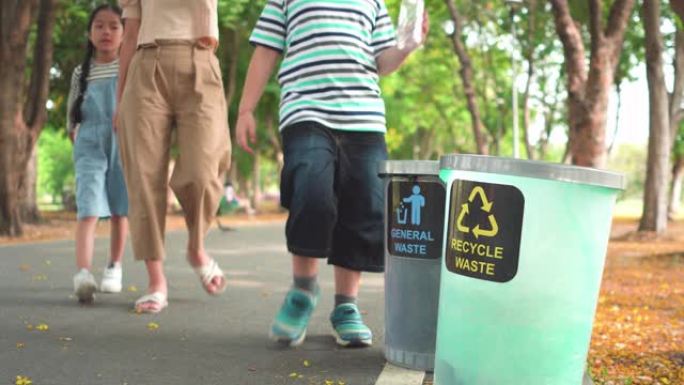 前视图: 周末阳光明媚的日子，亚洲家庭，母亲，兄弟和姐妹在公园的回收站中步行并分离透明塑料瓶作为回收