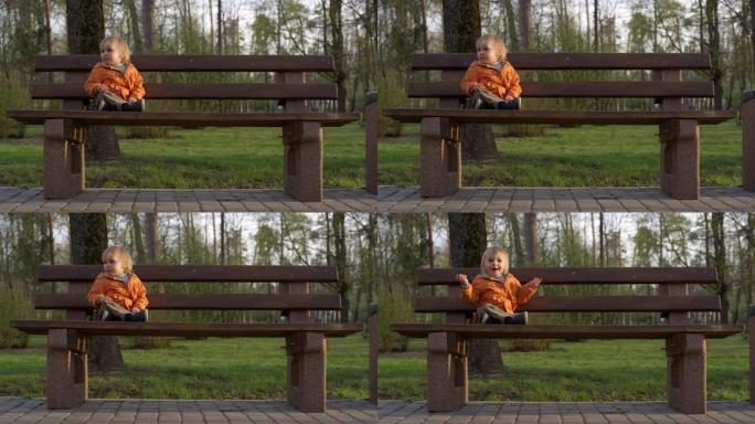 小男孩坐在公园的木凳上。蹒跚学步的男孩在森林背景下微笑
