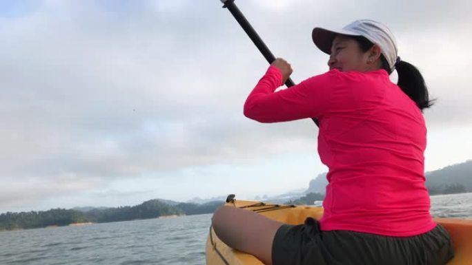 亚洲妇女在早晨的热带大湖中划皮划艇并向朋友挥手。放松运动