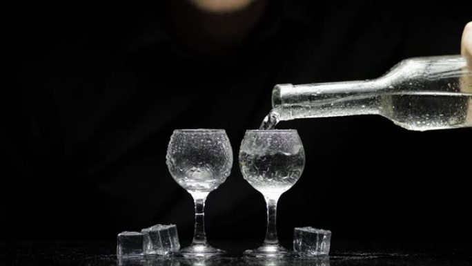 酒保把冷冻伏特加从瓶子里倒入两杯加冰的杯子里。黑色背景