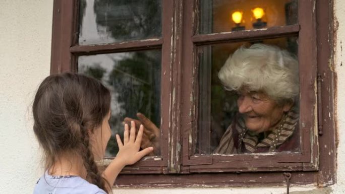 小女孩在大流行期间通过窗户拜访祖母