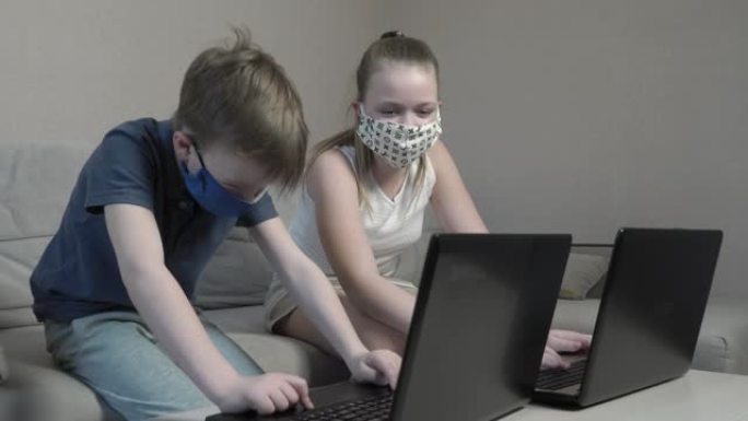 在COVID 19大流行期间，戴着防护面具的专注可爱的男孩和女孩使用笔记本电脑搜索信息互联网坐在家里