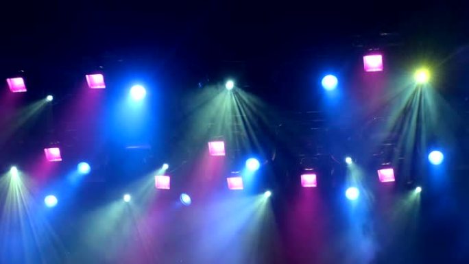 4k uhd手持灯光设备在演出时登上演唱会舞台。聚光灯下的光线穿过烟雾。蓝色和黄色紫色绿色光线