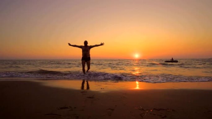 电影拍摄的肌肉发达的男性在日落时在沙滩上走出大海，双手伸出