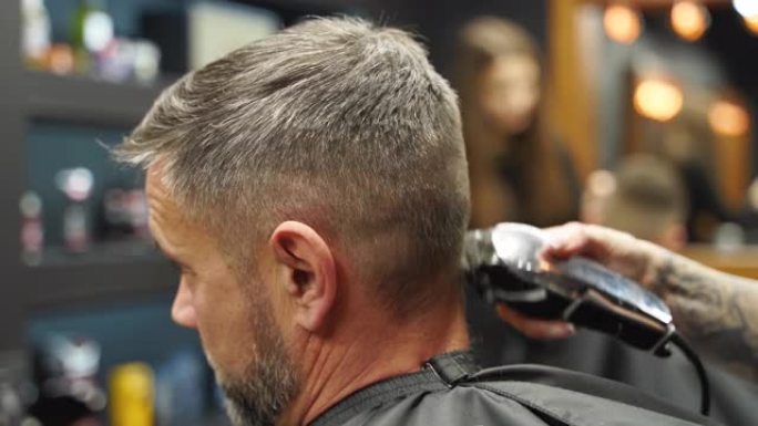 理发师在理发店用理发推子剪掉大胡子男人的头发。沙龙中的男士发型和理发。用修剪器梳理头发。理发师在复古