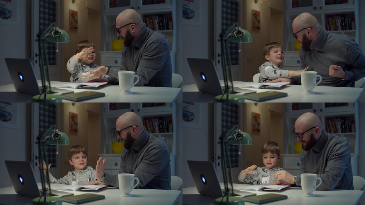 30多岁的年轻父亲在家里做在线作业时给儿子高五。大胡子的男人和小男孩用笔记本电脑在线学习。
