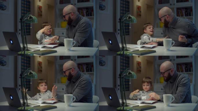 30多岁的年轻父亲在家里做在线作业时给儿子高五。大胡子的男人和小男孩用笔记本电脑在线学习。