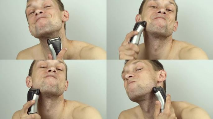 一个年轻英俊的男人用电动剃须刀刮胡须，在镜头前胡闹，做着可笑的鬼脸。