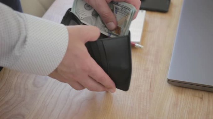 男手将钱数百元钞票放入工作桌上的皮革钱包，特写镜头