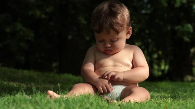 可爱的婴儿坐在大自然的户外。婴儿蹒跚学步的男孩通过触摸了解世界