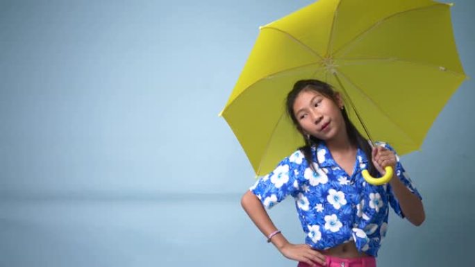 快乐的亚洲女孩使用蓝色背景的黄色雨伞，慢动作。