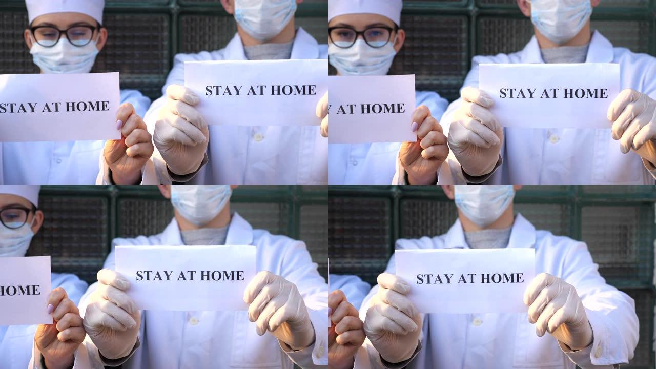 男性和女性医生拿着一张带有铭文的照片，在冠状病毒流行期间呆在家里。医务人员展示了具有自我隔离吸引力的