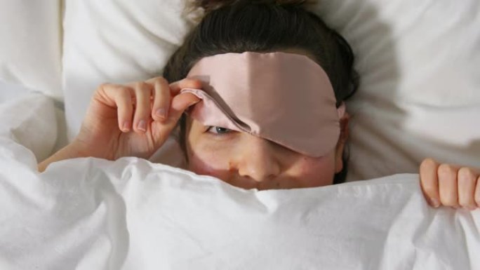 在毯子下的床上戴着眼睛睡眠面罩的女人