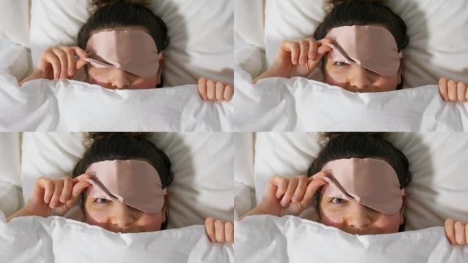 在毯子下的床上戴着眼睛睡眠面罩的女人