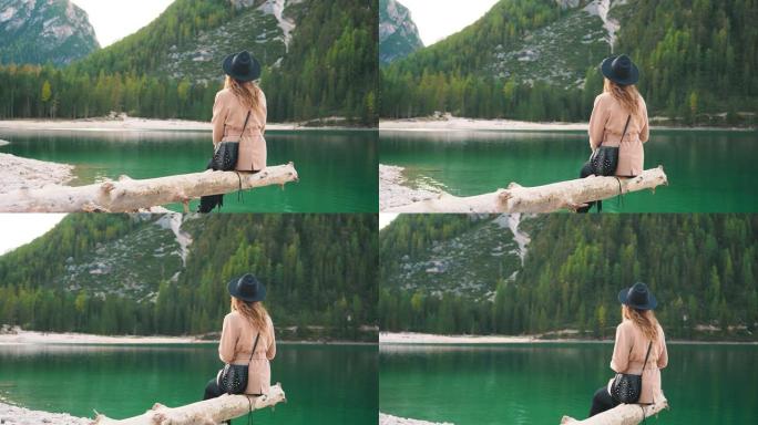 神秘的金发女人。坐在水湖上的峡谷上，游客放松，米色外套，黑色时尚帽子。明亮的绿色自然，山间针叶树，没