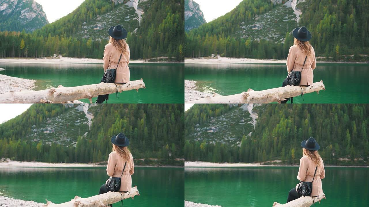 神秘的金发女人。坐在水湖上的峡谷上，游客放松，米色外套，黑色时尚帽子。明亮的绿色自然，山间针叶树，没