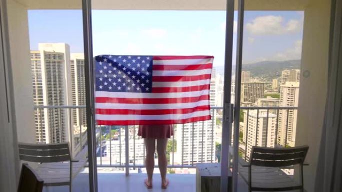 带着美国国旗的女人站在阳台上，以4k慢动作60fps的速度看着夏威夷檀香山的威基基海滩