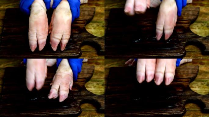 戴着橡胶手套的人的手在木制厨房板上用猪蹄滑稽地敲打。