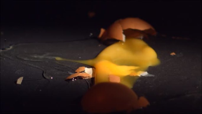 鸡蛋在黑色瓷砖表面以慢动作掉落和破碎。每秒高速1600帧。