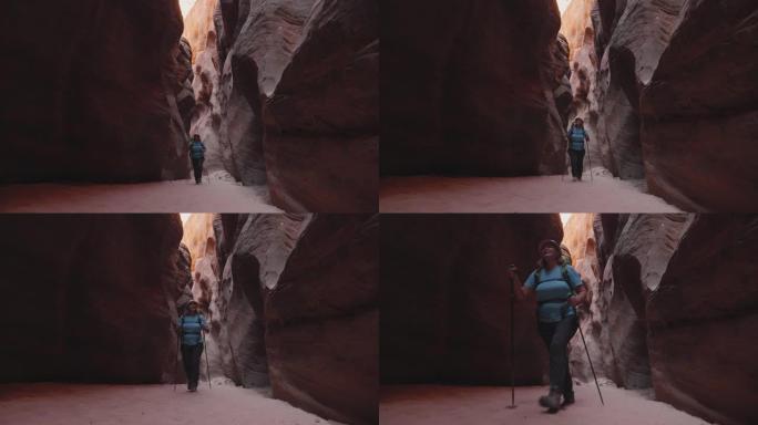 游客在带有橙色光滑岩石的深槽峡谷的干燥河床上徒步旅行