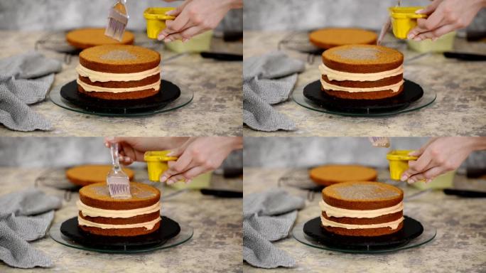 无法辨认的女性糖果手在厨房用硅烹饪刷用甜焦糖糖浆浸泡海绵蛋糕，特写。