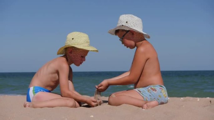 和孩子们一起在海上休息。沙子从手掌倒入孩子的手掌。海边两个戴着帽子的男孩。