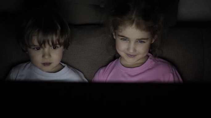 在笔记本电脑上看电视时，给小孩子画像。男孩和女孩在客厅的笔记本电脑上观看卡通。概念电子游戏，娱乐，情