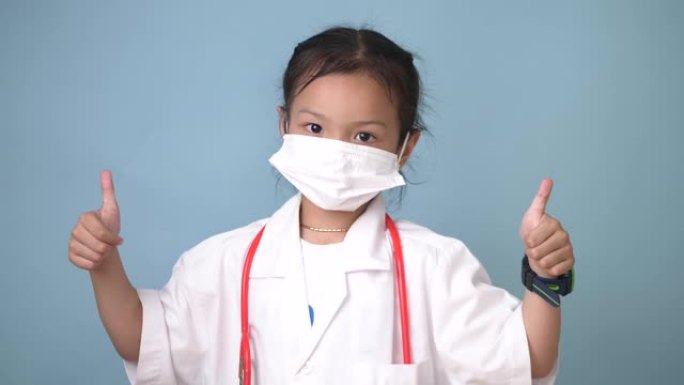 穿着蓝色背景大拇指的医生制服快乐的亚洲女孩。