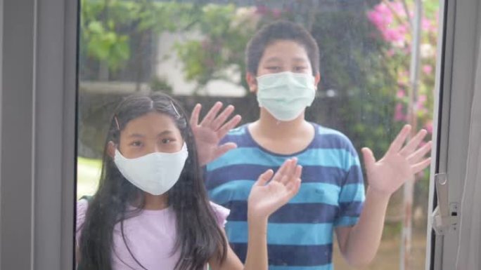 新型冠状病毒肺炎期间戴着面具的亚洲男孩和女孩从窗外问候