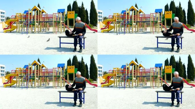 老人在空荡荡的儿童公园里和狗在长凳上看书