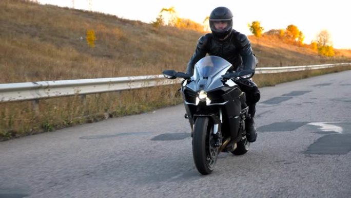 戴着头盔的男子在高速公路上骑着现代运动摩托车。摩托车手在乡间小路上骑摩托车。旅途中开车的人。自由和冒