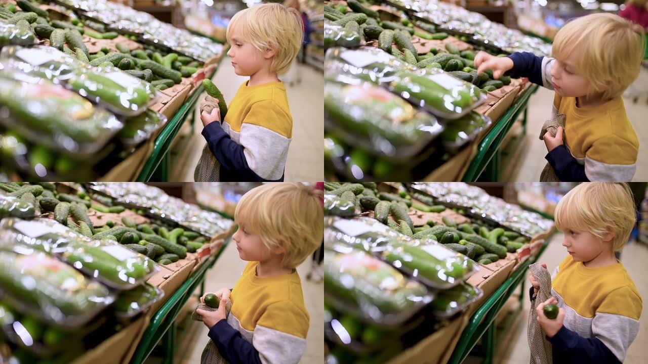 可爱的小男孩选择新鲜的有机黄瓜，然后放入食品店或超市的网状购物袋中。有孩子的年轻家庭的健康生活方式。