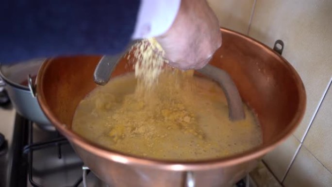 在家准备传统的冬季食物，意大利美食和古老的乡村食谱。男子用沸水和自动金属桨搅拌黄粥倒入库珀大锅中的玉