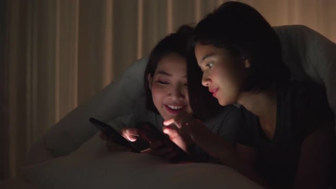 侧视图: 年轻的亚洲美女和朋友玩得开心，躺在公寓的床上，工作后通过电话放松，在互联网上分享，带着积极