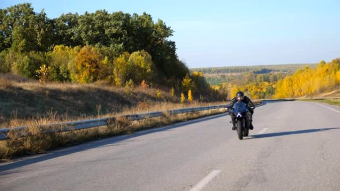 戴着头盔的年轻人在高速公路上快速骑现代运动摩托车。摩托车手在乡间小路上骑摩托车。旅途中开车的人。自由