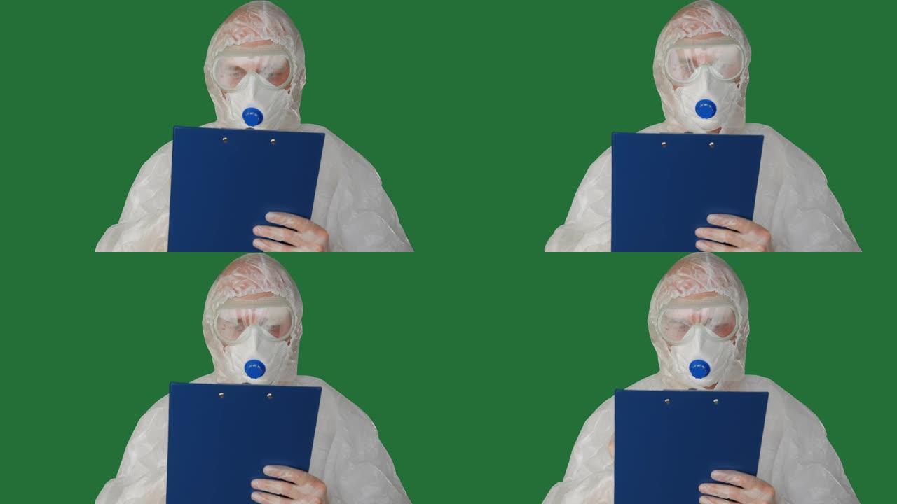 医务人员穿着防护服，在夹板上写面具。穿着安全服和面具的男人在绿色背景的剪贴板上写字。医生穿着防护服检
