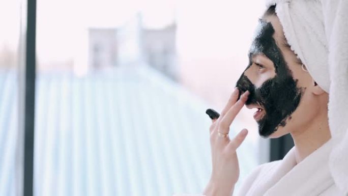 用毛巾包裹头发的漂亮女人正在脸上涂上黑色面具
