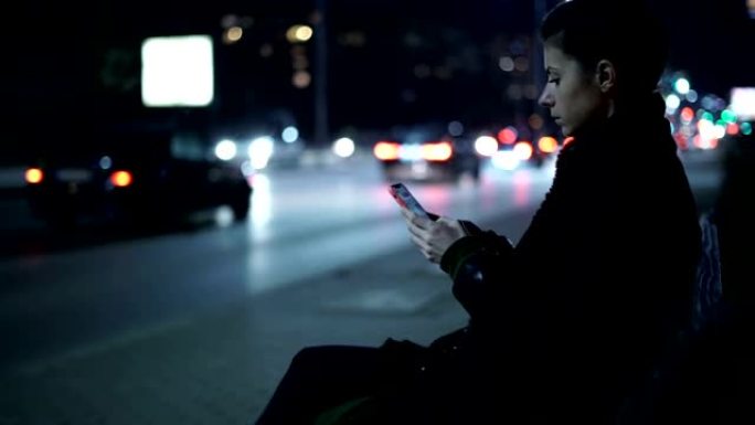 孤独的女人晚上在街上使用手机，夜间交通经过