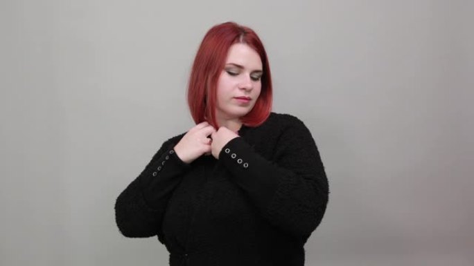 穿着黑色毛衣的红发胖女人时尚女人在扣眼里扣一个纽扣