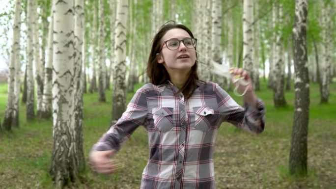 一个年轻女孩在森林里摘下了医用口罩。快乐的女孩走在白桦林里。大流行的结束。