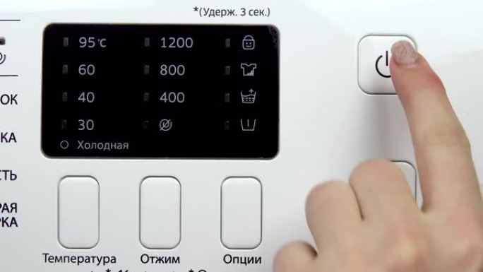 一个女人按下洗衣机的电源按钮。手特写。翻译: “冷，温度，拧干，选项，保持3秒”