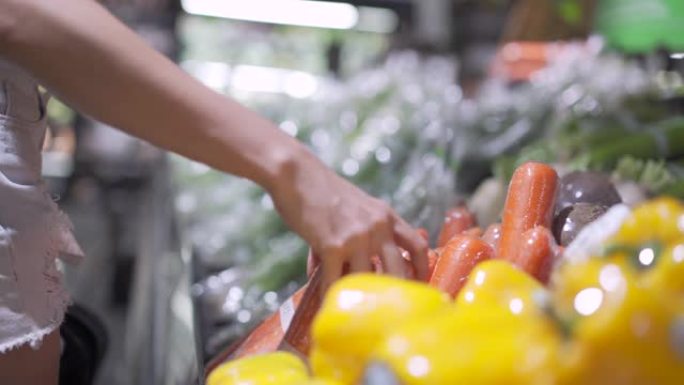 女人从超市货架上选择胡萝卜，储备食物，站在杂货店冷却货架前，新鲜蔬菜，生活方式，有机产品，蔬菜健康食