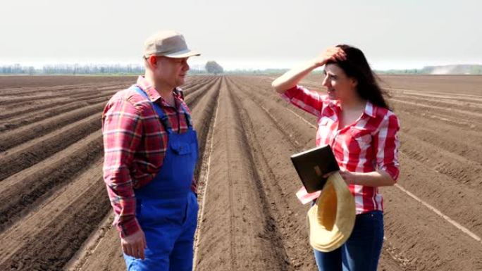 农民和农艺师站在田间的土壤行之间，用数字平板电脑谈论马铃薯栽培的质量。握手。现代农业。春天阳光明媚的