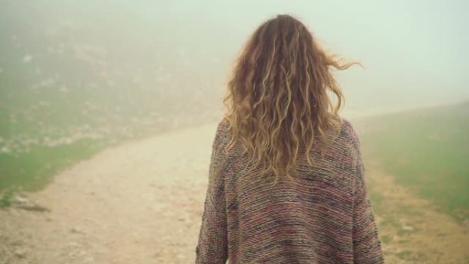 美丽的年轻女子，长长的波浪形金发在风中飞翔，走在蒙特巴尔多峰顶的石路上。转过身来，笑容满面享受干净的